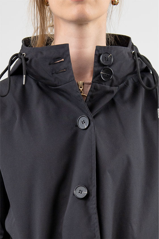 A close-up of a person wearing a stylish black looselyboho ONYX BLACK WINDBREAKER with a high collar and two drawstrings. The top half of the person's face is out of the frame. The windbreaker, made from lightweight water-resistant material, has four black buttons visible along the front.