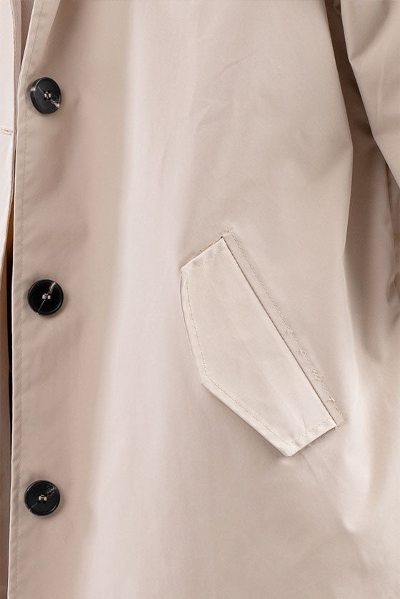 Close-up of a beige trench coat showing the side pocket and four black buttons. The fabric appears smooth and slightly shiny, suggesting it's a stylish BISCUIT BEIGE WINDBREAKER crafted from lightweight water-resistant material by looselyboho.